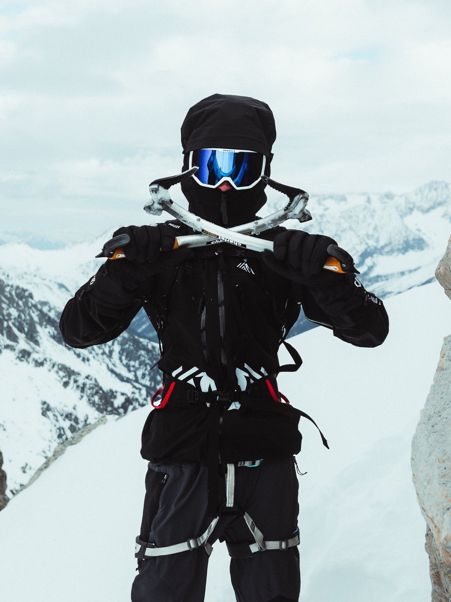 Climber holding ice tools while wearing the black Manaslu Summit Shell alpine hardshell jacket in alpine snow